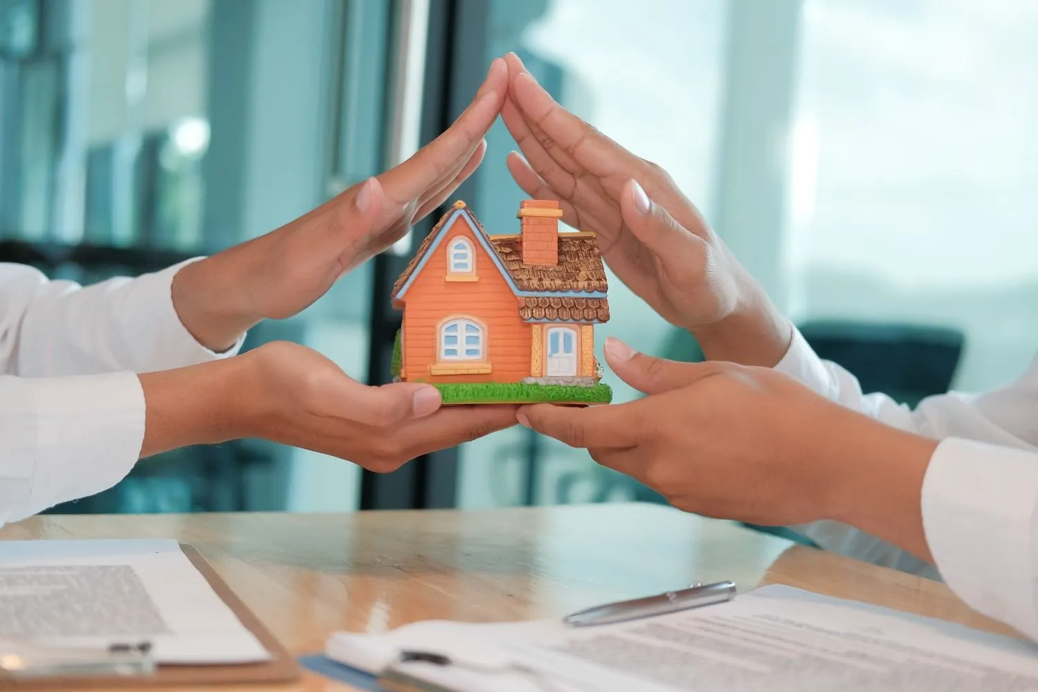Two hands forming a roof shape above a small model house