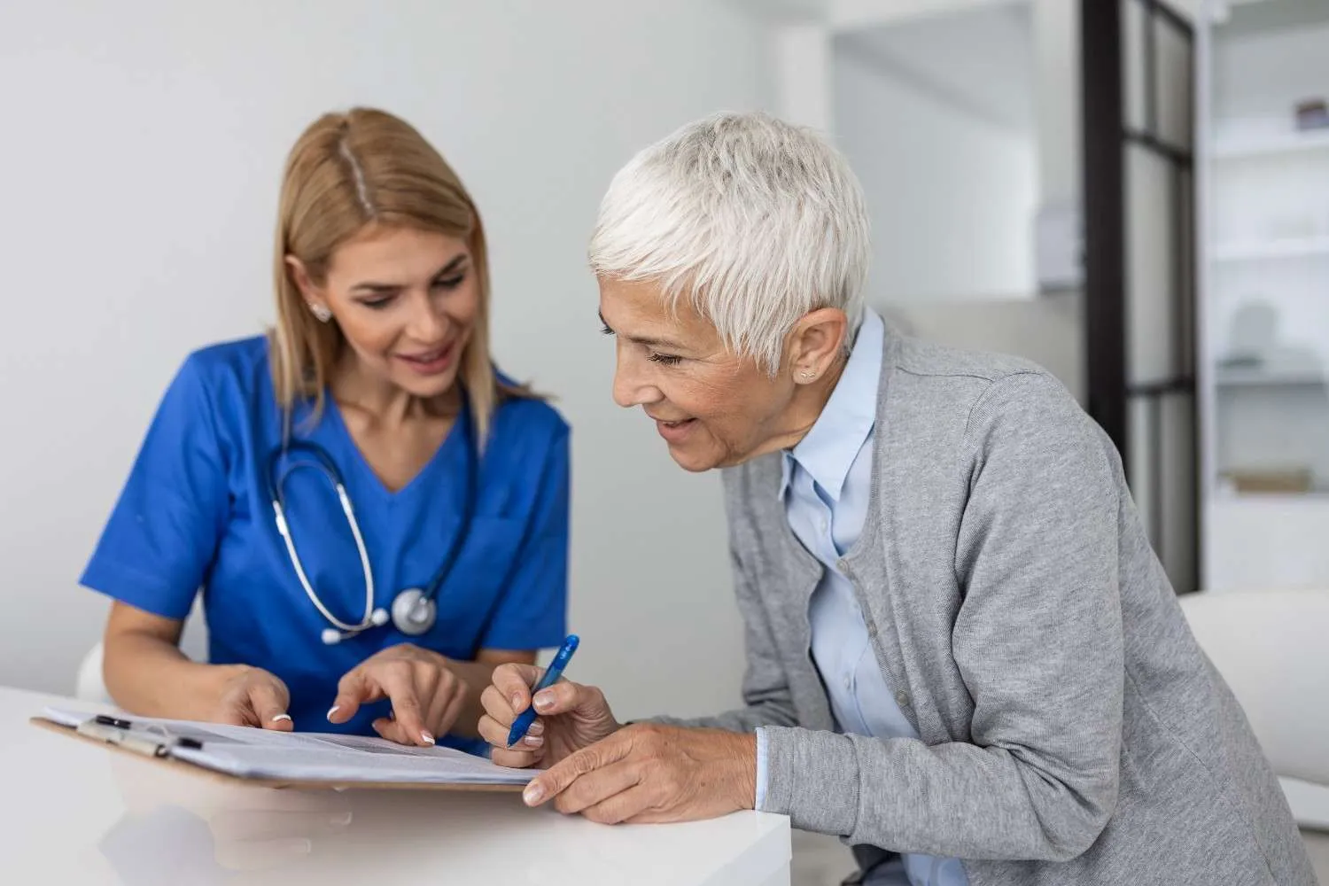 An older woman filling in a health form while a nurse points to a line